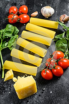 The concept of cooking cannelloni pasta. ingredients Basil, cherry tomatoes, Parmesan, garlic. Black background. top view