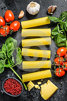 The concept of cooking cannelloni pasta. ingredients Basil, cherry tomatoes, Parmesan, garlic. Black background. top view