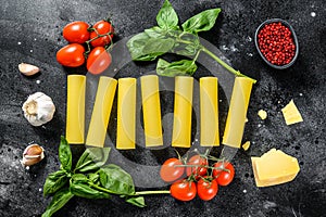 The concept of cooking cannelloni pasta. ingredients Basil, cherry tomatoes, Parmesan, garlic. Black background. top view