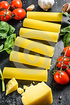 The concept of cooking cannelloni pasta. ingredients Basil, cherry tomatoes, Parmesan, garlic. Black background. top view