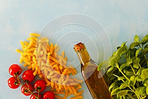 The concept of cooking pasta with pesto. Spaghetti, tomatoes, basil, a bottle with olive oil on a blue background. Place for text