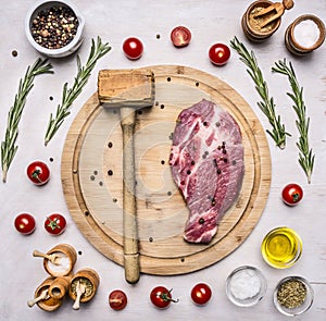 Concept cooking pork steak hammer for meat, seasoning, rosemary, parsley, oil and salt, are laid out around a wooden cutting board