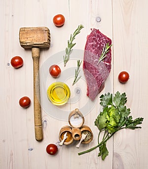 Concept cooking raw beef steak, rosemary, wooden hammer for beating the meat, oil, herbs and spices wooden rustic background to