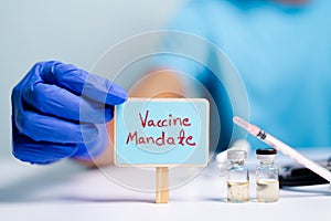 Concept of coronavirus or covid-19 vaccine mandate, showing with doctor hands with gloves by placing sign board next to vaccine