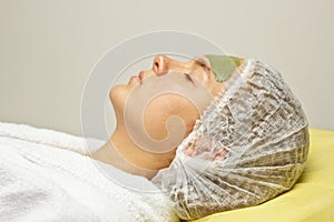 The concept of cosmetology. Close-up of a beautician applying a green mask with a brush on a woman`s face