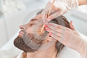 Concept of cosmetology and facial. A woman beautician makes face and beard modeling for a man waxing epilation
