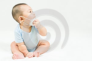 Concept covid-19 coronavirus pandemic.Portrait of cute little 5months old asian baby boy pulling a medical mask in blue bodysuit