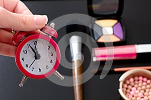 Concept cropped image with cosmetic and make up products. Quick make-up. Red retro clock. Selective focus