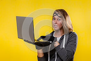 The concept of cybercrime and hacking. Portrait of a woman in black gloves and a mask on her head, who is holding a laptop. Yellow