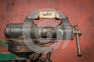 Vice grip tool squeezing a plank with the word ado photo