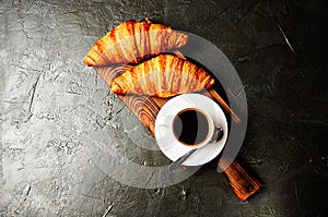 Concept of a delicious breakfast, croissants and espresso on a dark wooden board, on gray concrete, view from the top, flat lay