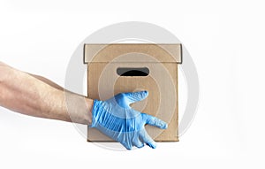 Concept of delivery of goods during quarantine. Young man in blue gloves holds cardboard box in his hands on white background.