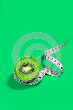 Concept diet and healhty lifestyle - kiwi and tape measure on trendy green blue background.