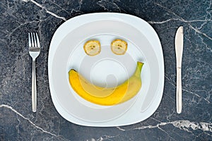 The concept of diet and healthy eating. Smile of a banana and two slices on a white platter, top view