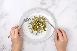 The concept of diet and weight loss. Women`s hands with a fork and a table knife over a plate of green peas