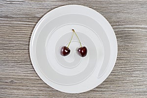 Concept of dieting and healthy eating. Red juicy cherries on white round plate. Wooden background, top view starving starvation we