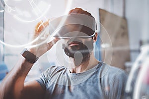 Concept of digital screen,connection and interfaces.Young beraded hipster enjoyingvirtual reality glasses in modern