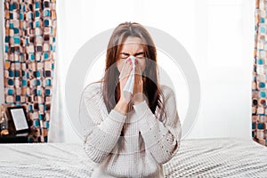 The concept of diseases and seasonal colds. A young brunette woman blows her nose in a handkerchief. Next to it are a thermometer