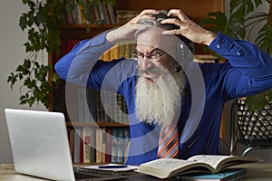 Concept of distance learning. Frenzied teacher tutor looking at laptop and clutching his head, selective focus