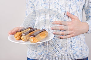 Concept of eating too much sweet food. Cropped close-up photo of woman holding plate with delicious glazed cupcakes holding hand