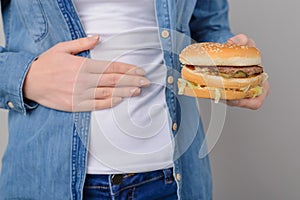 Concept of eating unhealthy food. Woman holding fatty hamburger