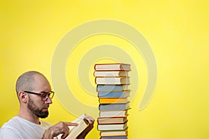 Concept of education. A bald man with a beard and glasses, holding a book and reading it intently. Nearby is a stack of books.