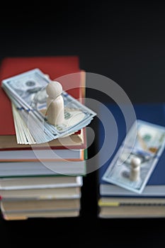 Concept of education and income. Wooden figures dollars and books on a black background. vertical photo.