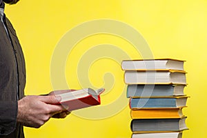 Concept of education. A man holds a book in his hands and reads it. Nearby is a stack of books. Yellow background