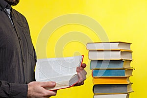 Concept of education. A man holds a book in his hands and reads it. Nearby is a stack of books. Yellow background. Copy space