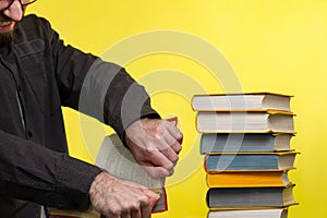 Concept of education. A man holds a book in his hands and tries to break it. Nearby is a stack of books. Yellow background