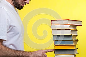 Concept of education. A man in a white t-shirt points to the penultimate book in the pile. Yellow background