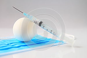 Concept of egg based manufacturing of a vaccine. Egg and hypodermic needle on a blue mask