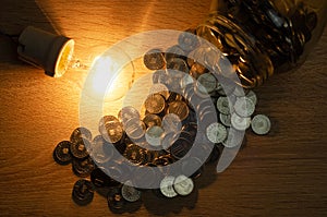 Concept of electricity consumption, in these times of crisis, represented with a light bulb and scattered euro coins,