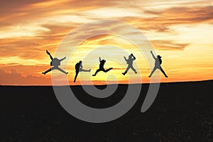 Concept of emotion. Silhouette of a happy group of people jumping at sunset in the mountain