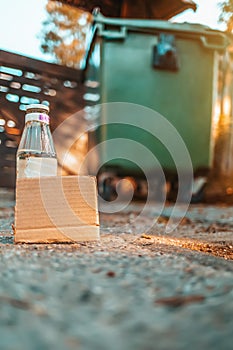 The concept of environmental pollution and waste sorting. A glass bottle stands on the ground in front of a dumpster. Near