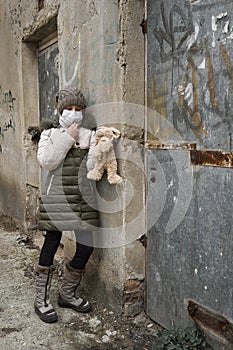 Concept of epidemic and quarantine - a girl with a face mask and a cuddly toy alone on the street in the city