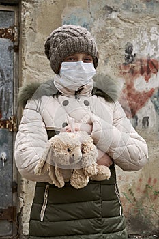 Concept of epidemic and quarantine - a girl with a face mask and a cuddly toy alone on the street in the city