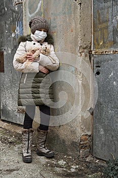 Concept of epidemic and quarantine - a girl with a face mask and a cuddly toy alone on the street in the city