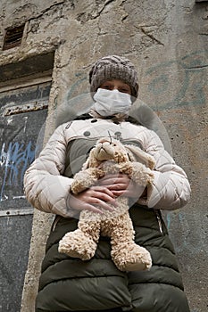 Concept of epidemic and quarantine - a girl with a face mask and a cuddly toy alone on the street in the city