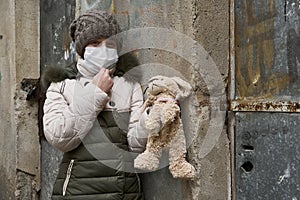 Concept of epidemic and quarantine - a girl with a face mask and a cuddly toy alone on the street in the city