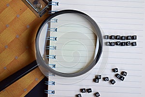 Concept of Expert Advice word on wooden cubes, on magnifying glass, books in background