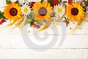 Concept of fall harvest or Thanksgiving day. Autumn composition with wheat ears, sunflowers and berries on white wooden table.