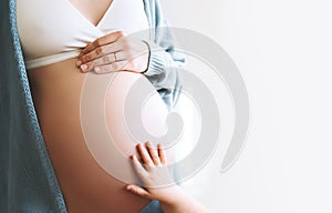 Concept of Family, Pregnancy, Motherhood, New Life. Close-up beautiful pregnant woman belly with her hand and little child hand.