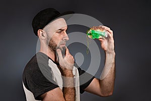 The concept of fast food and ecology. A man in a cap and a beard, holding a hamburger, and cautiously examines its plastic filling