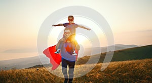 Concept of father`s day. dad and child daughter in hero superhero costume at sunset