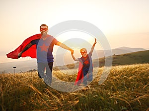 Concept of father`s day. dad and child daughter in hero superhero costume at sunset