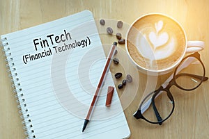 Concept fintech message on notebook with glasses, pencil and coffee cup on wooden table