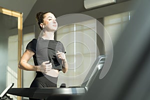 Concept fitness sport training lifestyle.Young woman running on a treadmill indoors. Young female running on the treadmill at