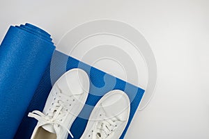 The concept of fitness, yoga, sports, healthy lifestyle. Top view photo of white sneakers and blue exercise mat against white