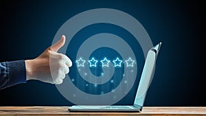 The concept of five stars. The best rating on the Internet. Hand showing thumbs up in front of laptop.